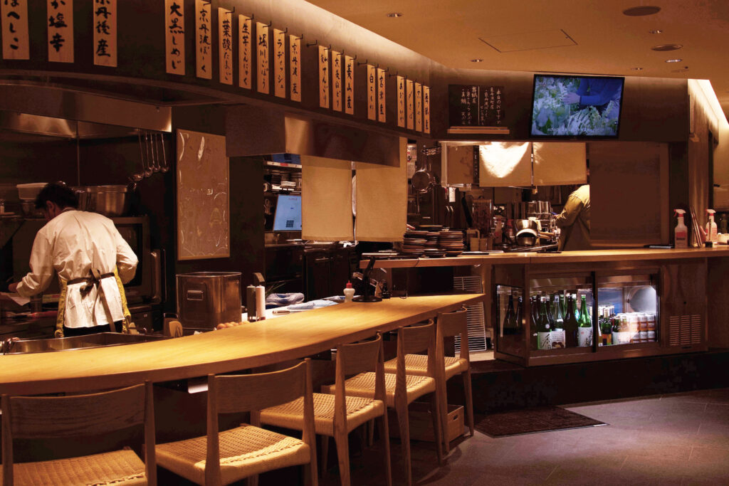26ダイニングの曲線カウンター席と、生産者映像が流れる店内モニター