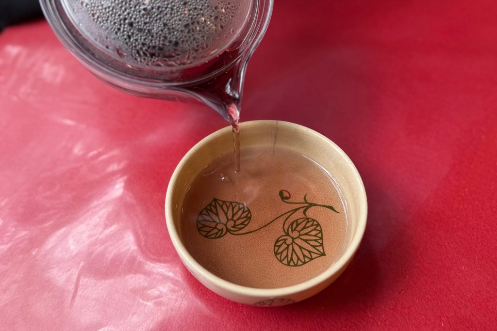 双葉葵の絵柄の器にまめ豆茶を注ぐ様子