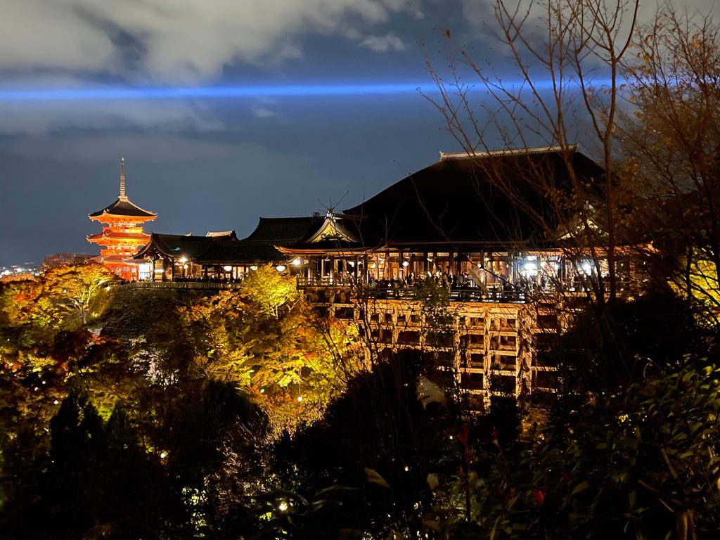 ライトアップされた清水寺の本堂と三重塔、夜空を横切る青い光